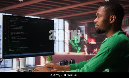 Male programmer types code on computer and running script, programming language. African american IT expert in modern loft fixing errors within the software, implementing new features. Camera A. Stock Photo