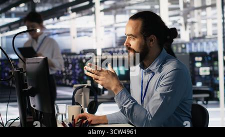 Data center technician discussing with coworker while doing AI software updates. Server room IT specialist and colleague chatting, optimizing infrastructure using artificial intelligence, camera A Stock Photo