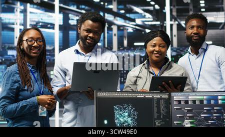 Smiling server hub engineers collaborating, using AI algorithms and node tree systems to categorize unstructured data. Colleagues use visual programming and natural language processing tools, camera B Stock Photo
