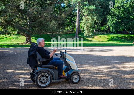 Elderly man using smartphone while seated on mobility scooter in a park Stock Photo