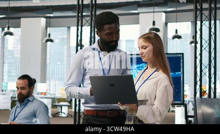 Junior dev and colleague in office reviewing AI system metrics, monitoring performance dashboards. Tech company programmer and young female engineer tuning neural networks, camera A Stock Photo