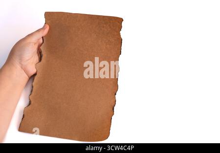 Old vintage dark burnt edges kraft paper. Hand holds blank kraft sheet on isolated white background, space for text, motion blur, selective focus Stock Photo