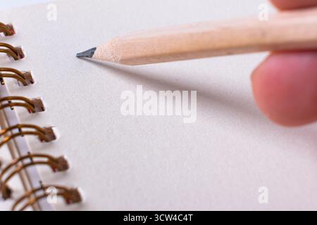 Close-up of hands writing down on the spiral notepad. Hand with wooden pencil preparing to write on blank notebook Stock Photo