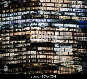 city office block high rise at night, lit up windows and work cubicles, urban lifestyle, modern stress and space pressure Stock Photo