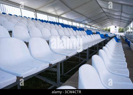 Empty white seats of tribune on sport stadium. Many empty plastic seats in rows in an outdoor stadium. Concept of fans, chairs for audience Stock Photo