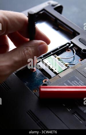 Closeup of technician hand working with screwdriver and laptop internal parts. The repair process shows concept of technology, tools and professional Stock Photo