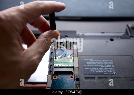 Technician hand installing or removing a computer component using a screwdriver inside laptop body. The photo illustrates concept of technology repair Stock Photo