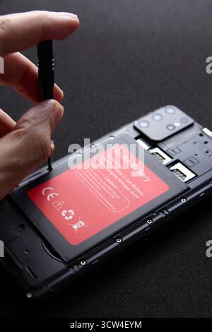 A closeup of technician hands using screwdriver to open smartphone for battery replacement. The image shows concept of technology service and repair p Stock Photo