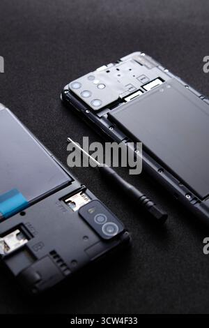 Disassembled smartphone with detached screen and screwdriver on black background. The minimal photo represents concept of technology repair and servic Stock Photo