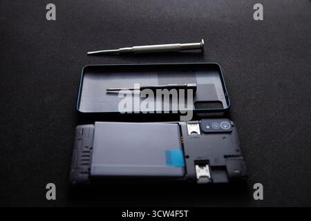 A disassembled smartphone with screwdriver and tools arranged neatly on dark background. The minimalistic composition shows technology repair concept Stock Photo