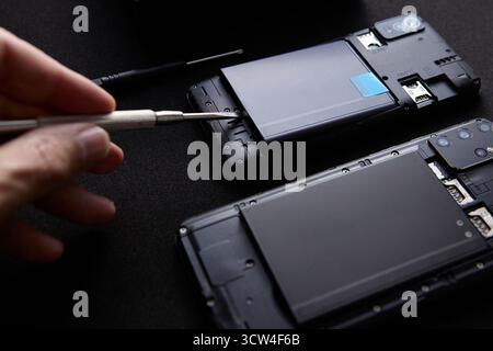 Closeup of hand using precision screwdriver to remove parts of a smartphone during repair. Studio image shows concept of modern technology maintenance Stock Photo