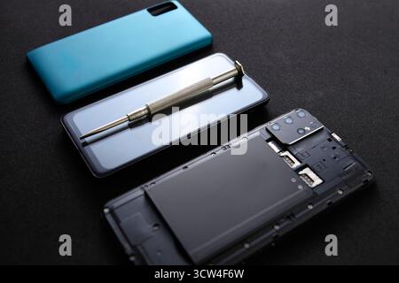 A smartphone, battery, and screwdriver are placed in order on a black table. The clean arrangement shows concept of technology repair and precision wo Stock Photo