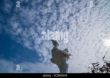 The sculpture at the Karon Beach roundabout in Phuket stands beneath a sky filled with small, fluffy clouds, gently diffusing the sunlight and casting Stock Photo