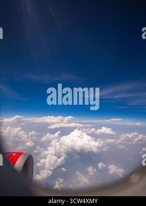 View from airplane window scattered white clouds floating above a vast landscape, with winding rivers below. The deep blue sky and soft cloud formatio Stock Photo