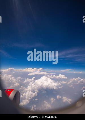 View from airplane window scattered white clouds floating above a vast landscape, with winding rivers below. The deep blue sky and soft cloud formatio Stock Photo