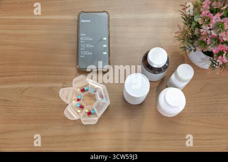 Elderly woman putting pills into pill box and set medication reminder alarm clock. Stock Photo