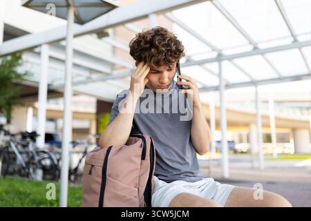 Stressed traveler guy touching head while talking on phone at airport Stock Photo