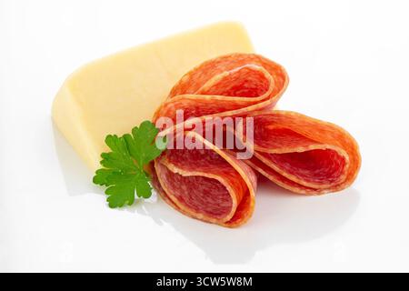 Close-up of thinly sliced Hungarian salami arranged beside a wedge of Edam cheese and a sprig of parsley on a white background, ideal for culinary and Stock Photo