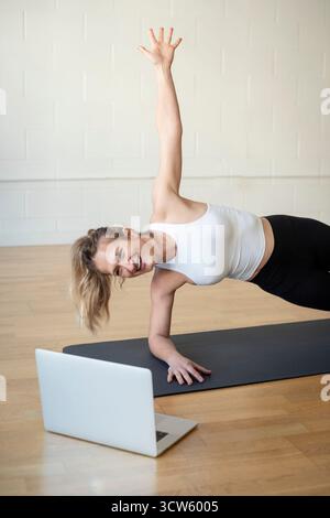 Woman doing virtual yoga session in side plank pose Stock Photo