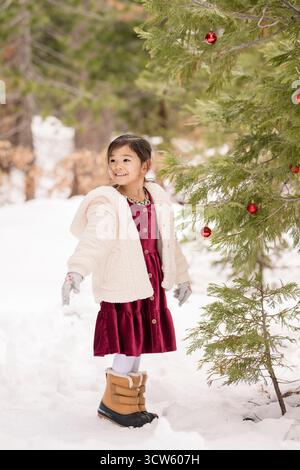 Smiling girl in cozy winter clothes admires a decorated pine tree Stock Photo