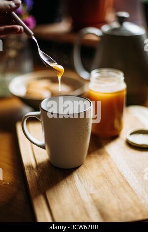 Honey dripping from spoon into cup Stock Photo