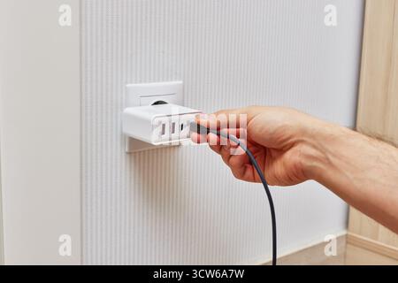 male hand insert a plug of the phone charger into socket at home Stock Photo