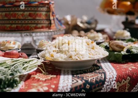 A large plate of pilaf with rice and raisins on a festive table. White rice with saffron and raisins in a plate against a bright red patterned tablecl Stock Photo