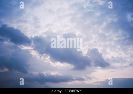 Dark-toned clouds float against a bright, empty sky. Subtle contrast and softness create a quiet visual tension. Shot on analog film. Stock Photo