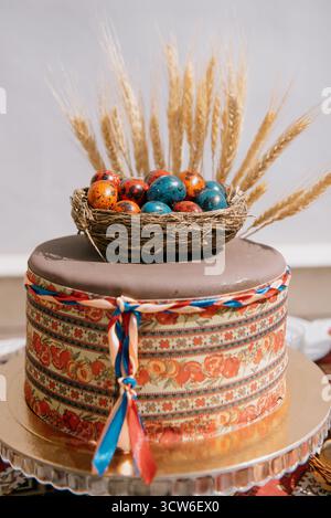 A festive cake decorated with a nest of brightly colored quail Easter eggs. An original Easter or spring cake with an artificial nest and wheat ears Stock Photo