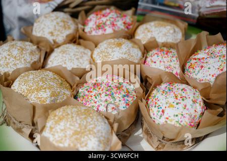 Lots of fresh Easter cakes with white icing and colorful sprinkles. A close-up of rows of Easter cakes wrapped in craft paper for sale at a store Stock Photo
