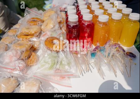 Colorful drinks, donuts, and candies for a children's party at the fair. A table with packaged donuts, bottled juices and candies for sale on the stre Stock Photo