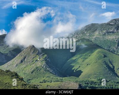 Cloud over green mountain range landscape - Majestic summer view of Picos de Europa mountain range with lush green slopes and dramatic cloud formation Stock Photo