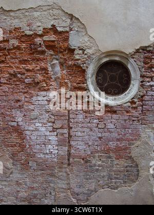 Rustic Red Brick Wall with Round Window - Close-up texture of an old, damaged red brick and plaster wall with a circular stone-framed window (oculus) Stock Photo