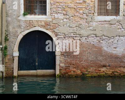 Old Venetian Water Door on Weathered Brick Wall - Close-up of a weathered red brick and plaster wall with a decaying arched water door (porta d'acqua) Stock Photo