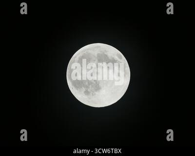 A crisp, detailed view of the glowing October full moon, showing clear craters and surface geology against a pitch black night sky Stock Photo