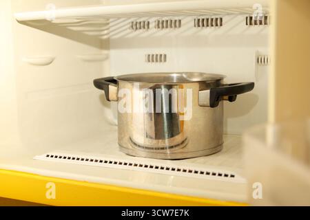 a frozen freezer or refrigerator compartment with thick layers of ice, using a saucepan of boiling water inside to melt the frost. Stock Photo