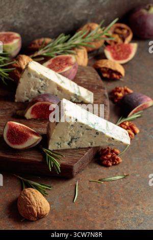 Blue cheese with fresh figs, rosemary, and walnuts on a vintage background. Stock Photo