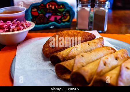 Traditional Salvadoran meal featuring golden fried taquitos and a crispy empanada, served with curtido (pickled cabbage slaw) and tomato salsa Stock Photo