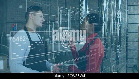 Discussing brewing data interface in black aprons amid steel tanks and piping in brewery facility. Craftsmanship, industrial, innovation, teamwork, te Stock Photo