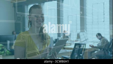Smiling woman wearing yellow blouse holding tablet with UI overlays in tech office with monitors. Collaboration, innovation, modern, dynamic, teamwork Stock Photo