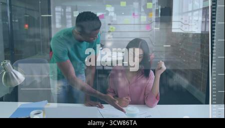 Pointing two colleagues collaborating over printed documents at office desk, showing sticky notes. Collaboration, teamwork, modern, professional, work Stock Photo