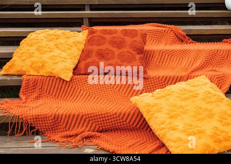 Soft orange pillows and knitted blanket placed on wooden surface creating cozy autumn atmosphere. Warm home decor concept symbolizing comfort and seas Stock Photo