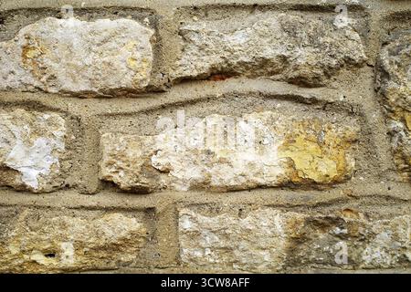 Rough-hewn stone wall in the Cotswolds, England featuring irregularly shaped sandstone blocks. Varied shades of beige, cream, and light yellow create Stock Photo