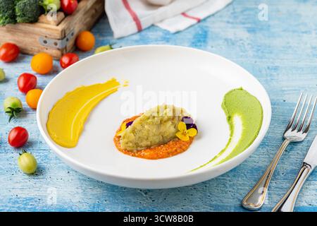 Eggplant puree with colorful sauces and edible flower garnish Stock Photo