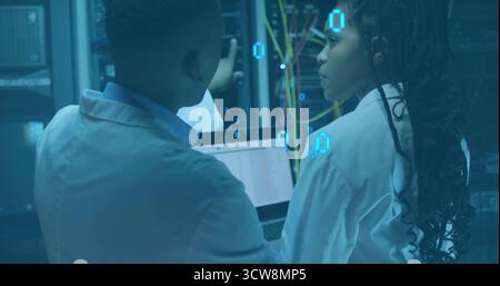 Two IT techs wearing lab coats inspecting server racks in data center, with network cables, laptop. Technology, innovation, data, security, connectivi Stock Photo