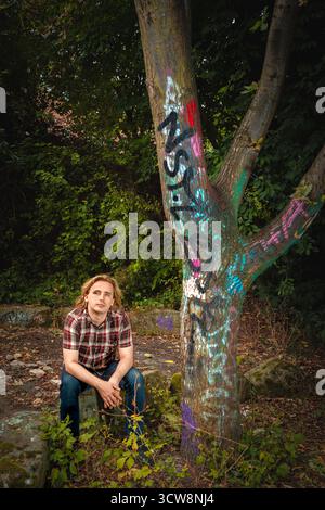 portrait of young man sitting, next to graffiti covered tree, Waythrough charity Stock Photo