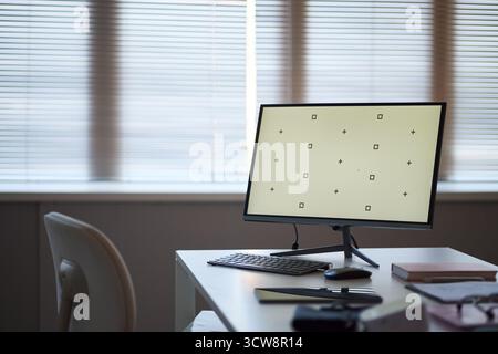 Blank modern desktop computer monitor standing on office desk with wireless keyboard and mouse, closed notebook and pen visible. Template, copy space Stock Photo