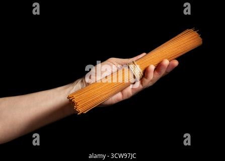 brown integrale spaghetti in hand isolated on black Stock Photo