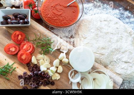 Top view of classic Italian pizza ingredients—mozzarella, flour, garlic, tomato sauce, olives, and onions—arranged for home baking preparation. Stock Photo