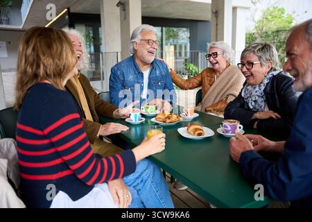 Happy group senior people laughing and enjoying coffee sitting at cafeteria bar table for breakfast Stock Photo